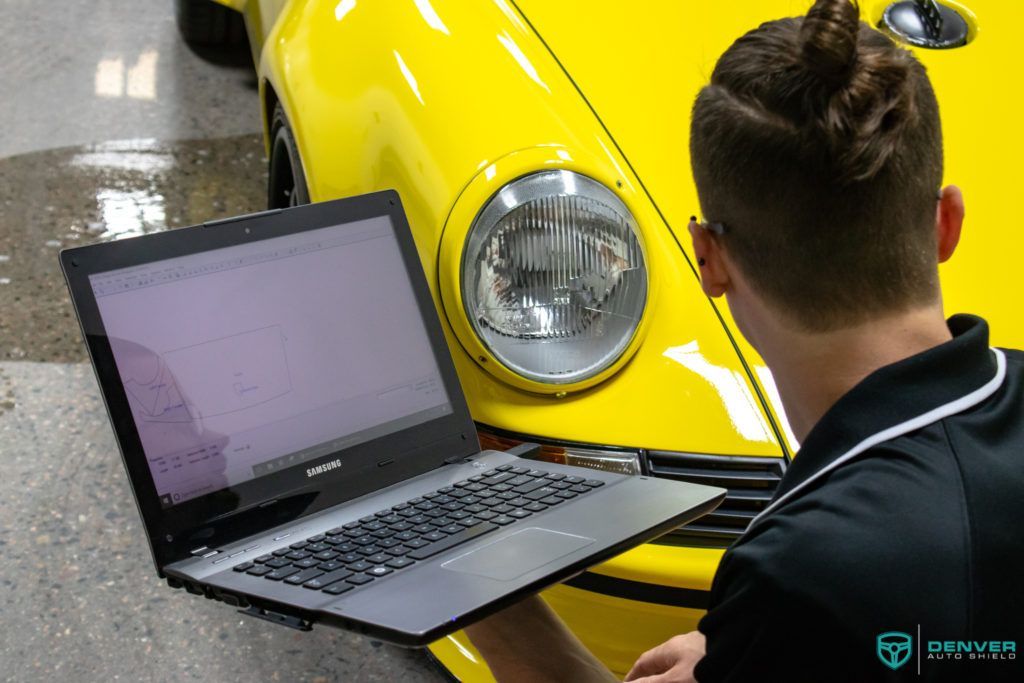 A man is using a laptop in front of a yellow car.