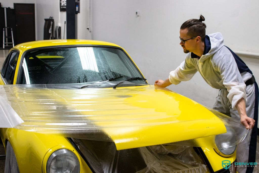 A man is wrapping a yellow car with plastic wrap.