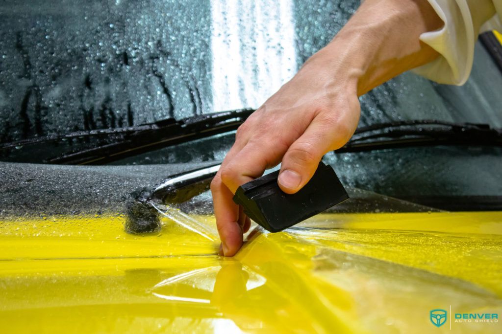 A person is cleaning a yellow car with a sponge.