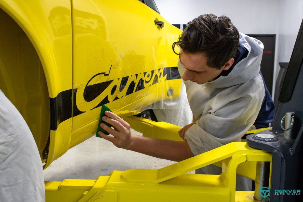 A man is cleaning a yellow car with a green cloth.