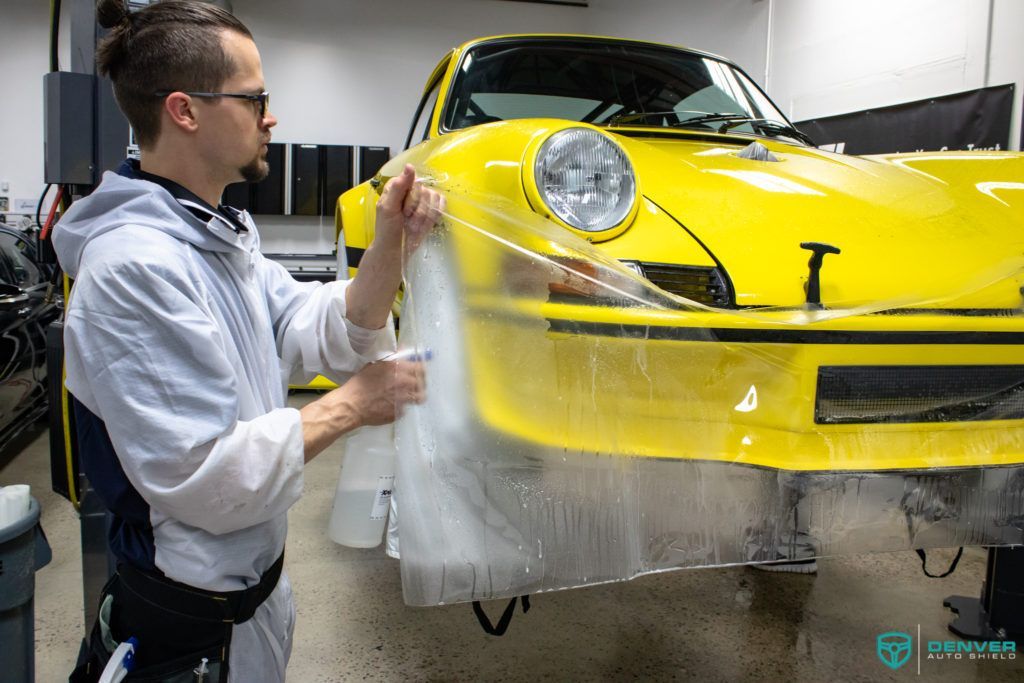 A man is wrapping a yellow car with plastic wrap.