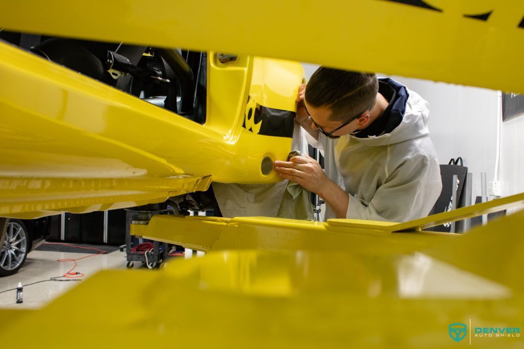 A man is working on a yellow car in a garage.