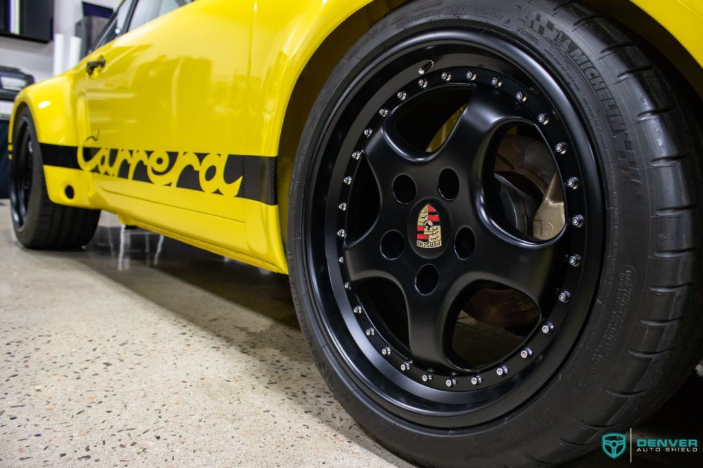 A yellow car with black wheels and tires is parked in a garage.