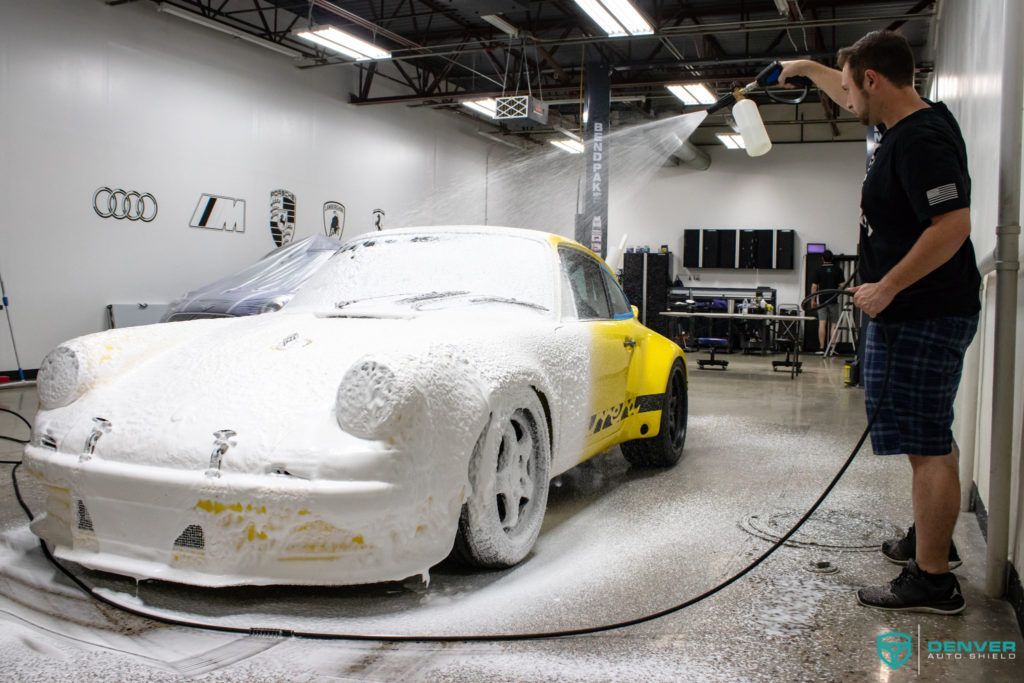 A man is washing a car with foam in a garage.