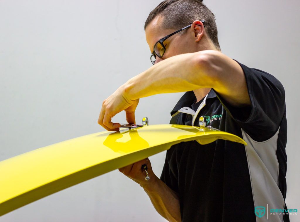 A man wearing glasses is working on a yellow piece of wood.