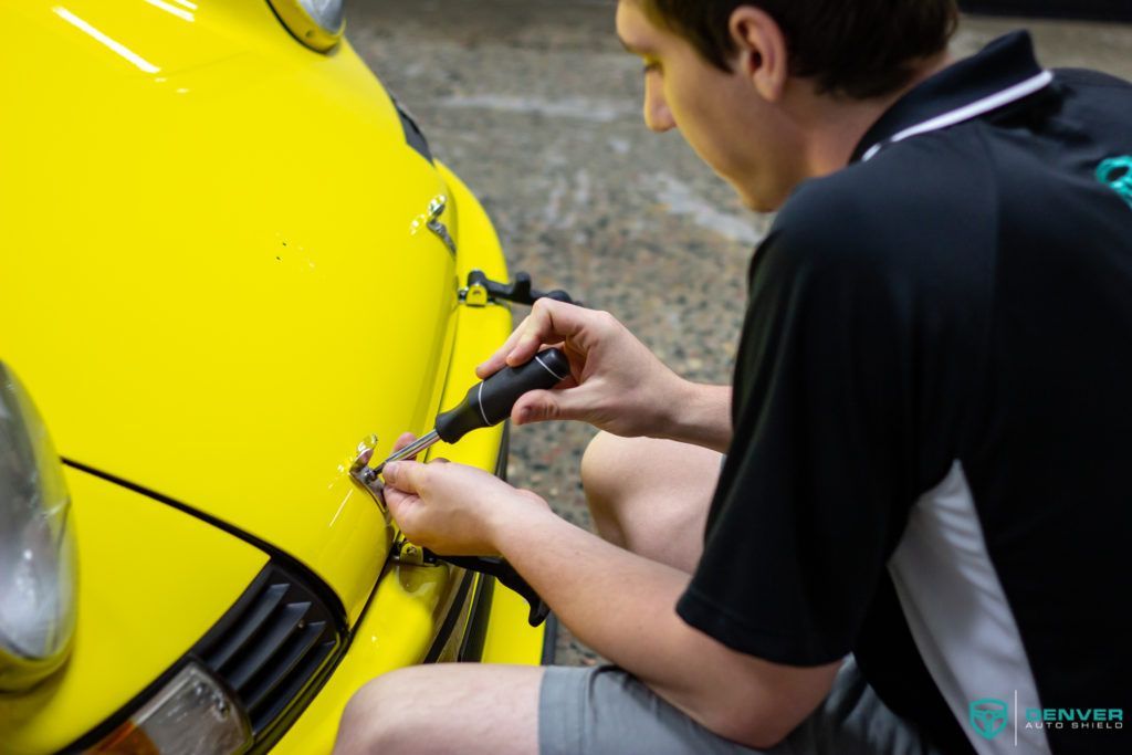 A man is working on the front of a yellow car.