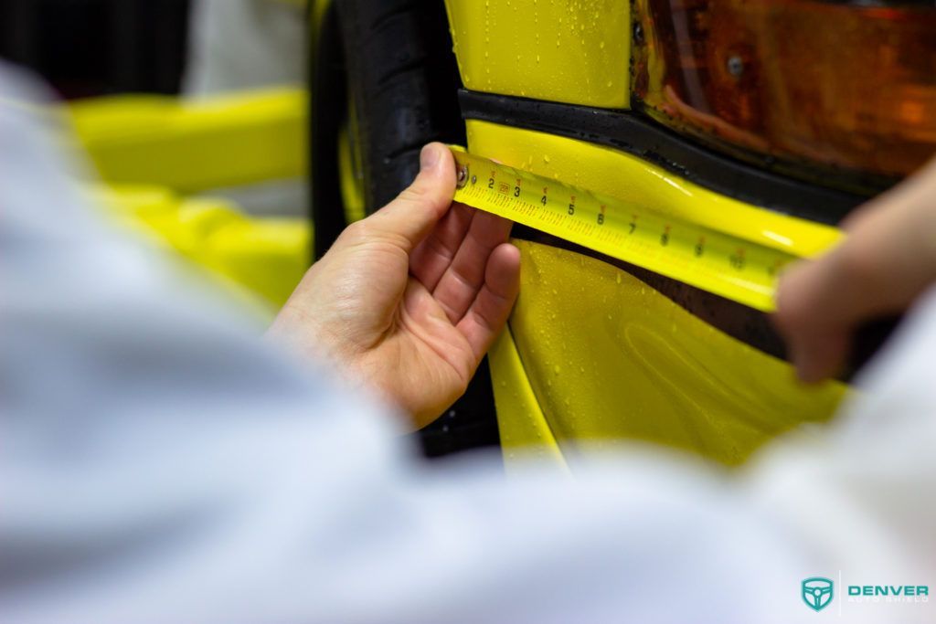 A person is measuring a yellow object with a tape measure.