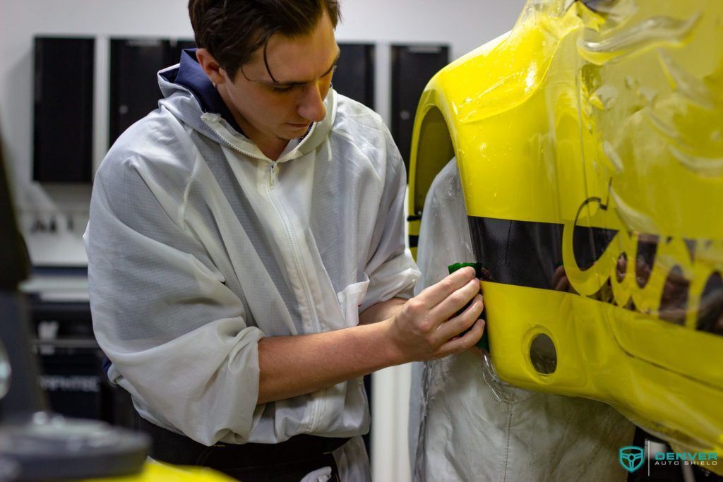 A man in a white coverall is working on a yellow car.