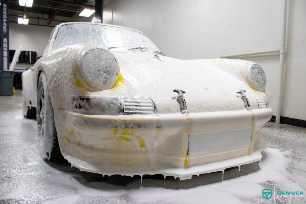 A white porsche is covered in foam in a garage.