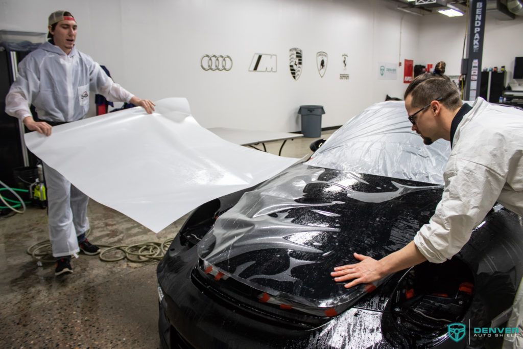 Two men are working on a black car in a garage.