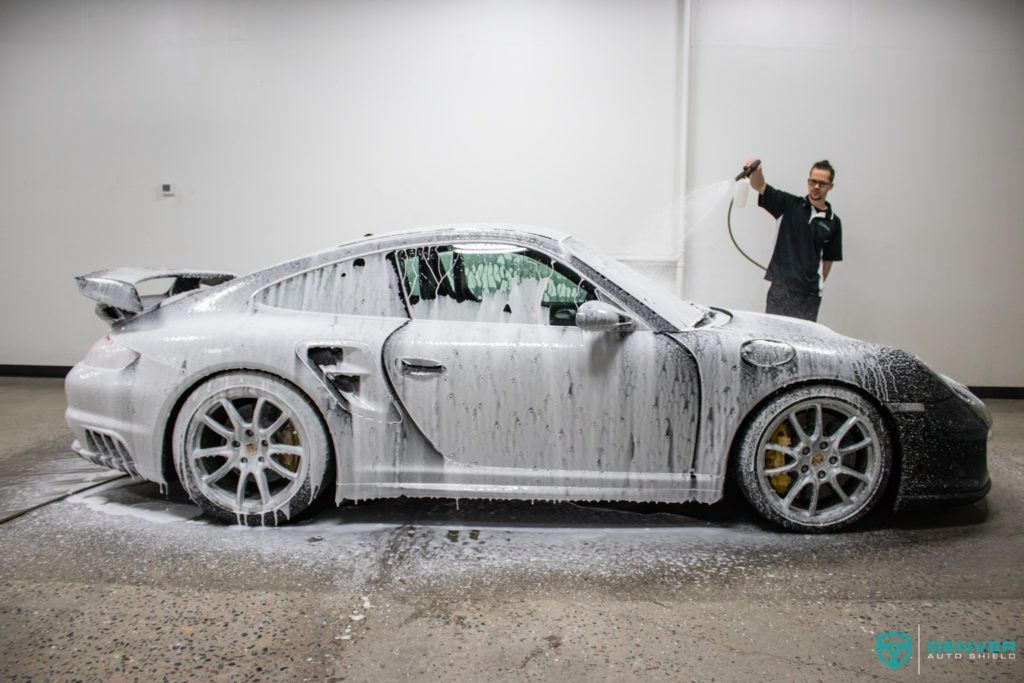 A man is washing a porsche with foam in a garage.