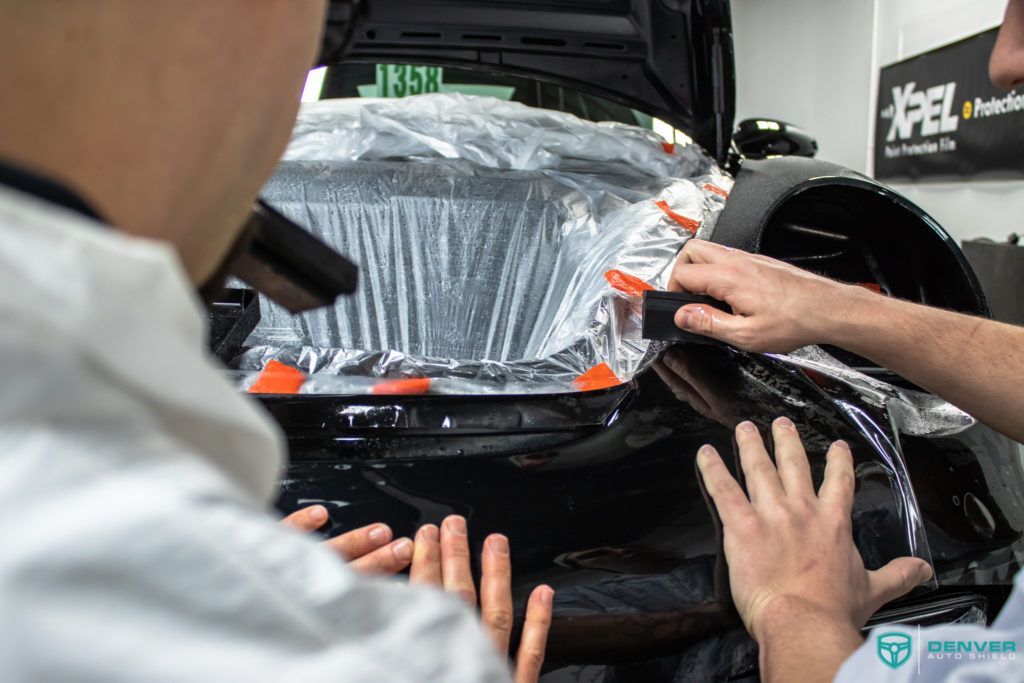 A man is covering a car with plastic wrap.