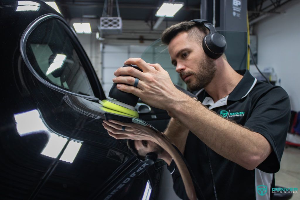 A man wearing headphones is polishing a black car.