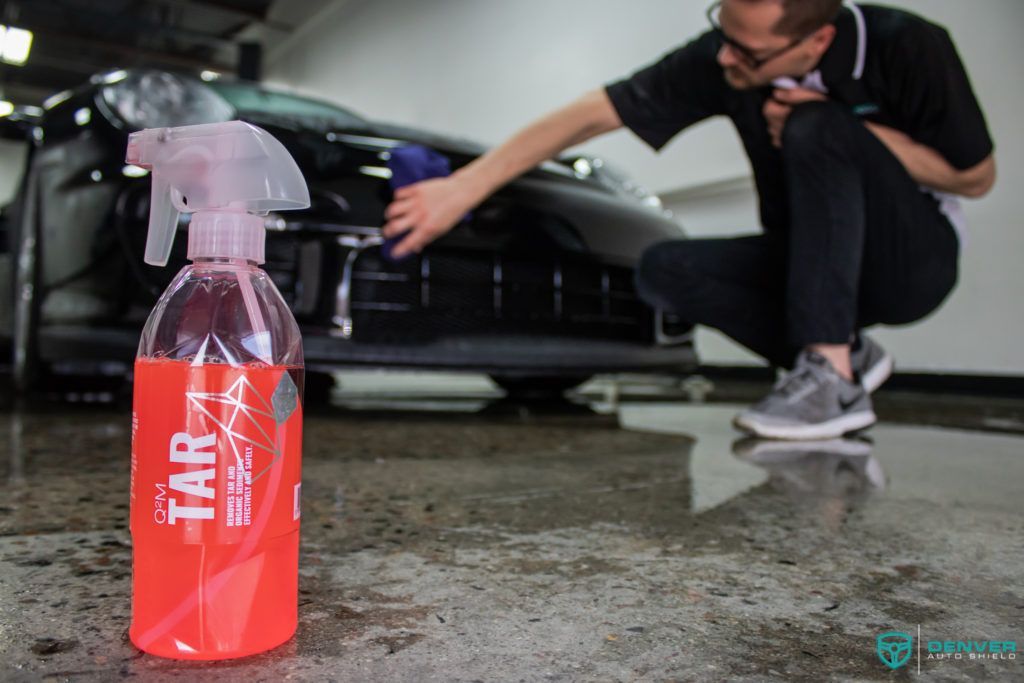 A man is kneeling down next to a bottle of tar spray.