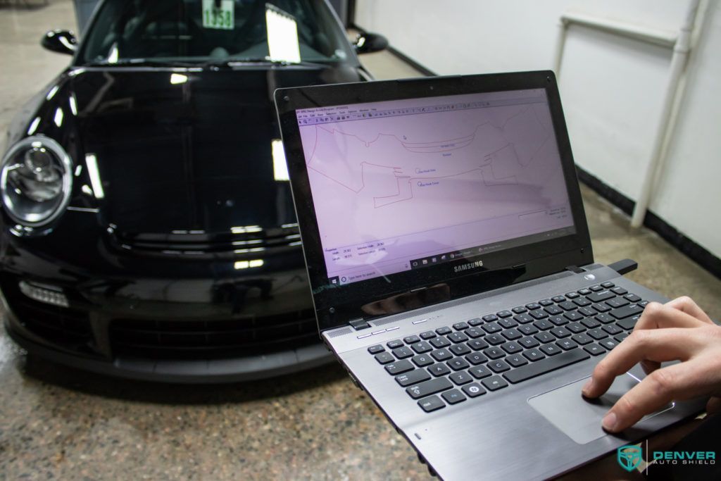 A person is typing on a laptop in front of a black car