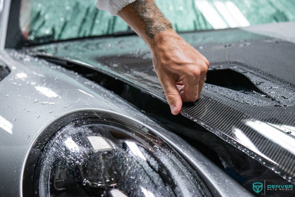 A person is applying a protective film to the hood of a car.