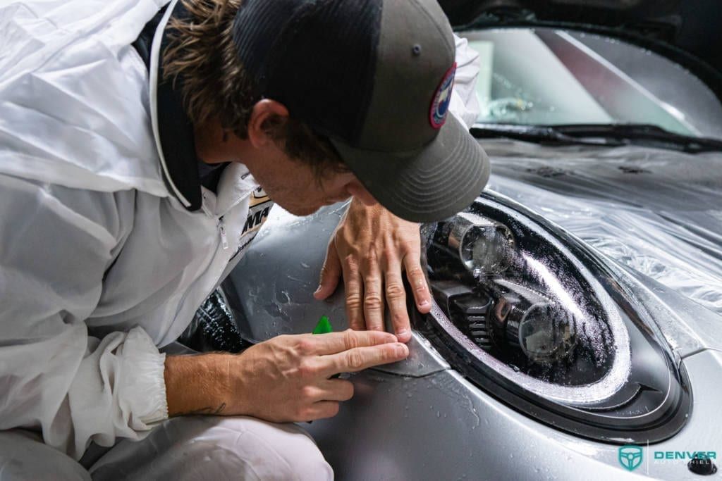 A man is applying a protective film to the headlight of a car.