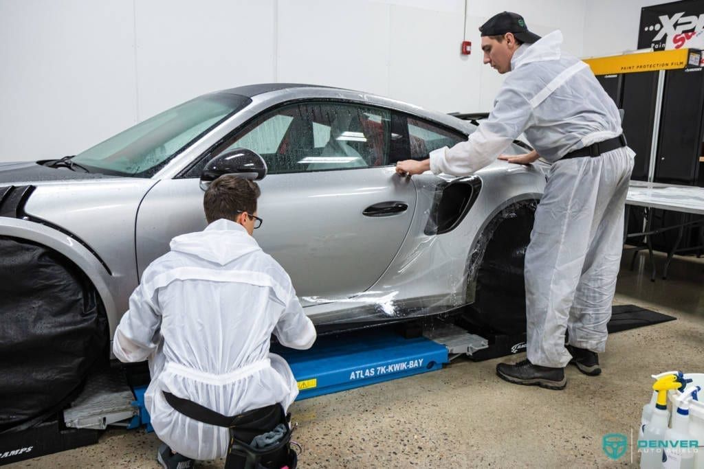 Two men are working on a silver sports car in a garage.