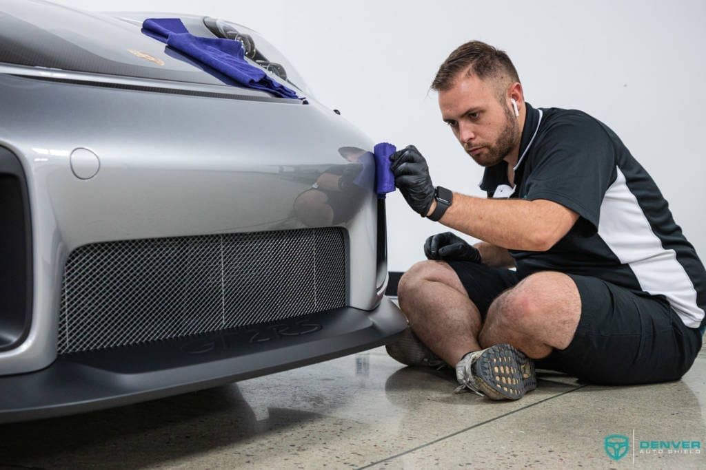 A man is sitting on the floor polishing the front bumper of a car.