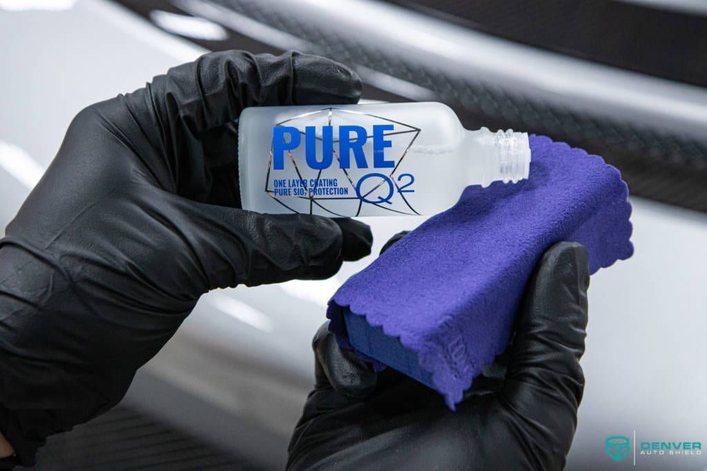 A person wearing black gloves is holding a bottle of pure and a sponge.