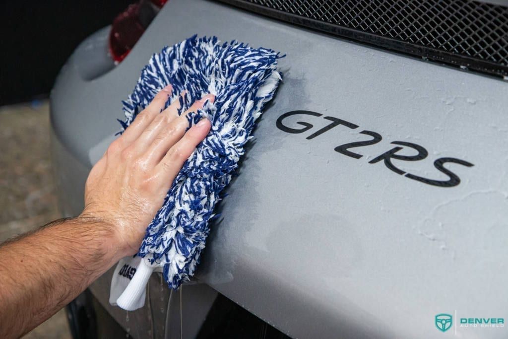 A person is cleaning a car with a mop.