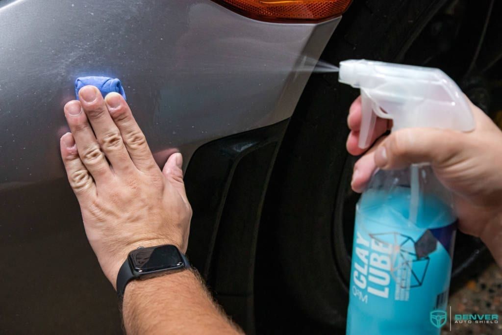 A person is cleaning a car with a sponge and a spray bottle.