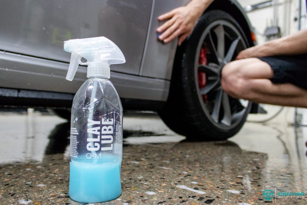 A person is kneeling next to a car with a spray bottle next to it.
