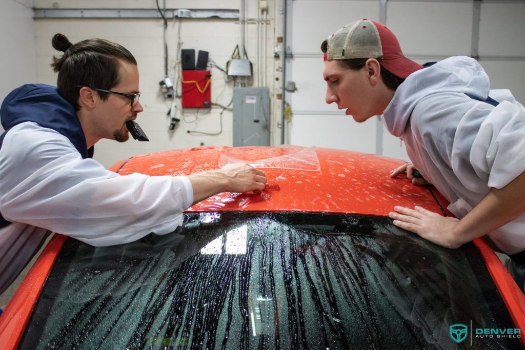 Two men are cleaning a red car in a garage.