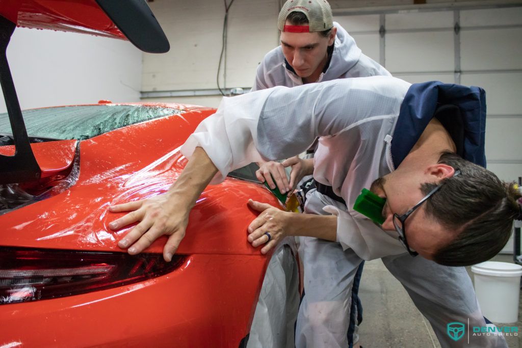 Two men are working on a red car in a garage.