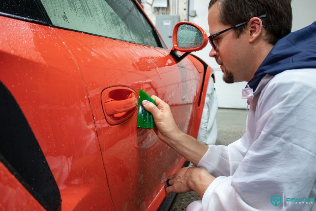 A man is cleaning a red car with a green sponge.