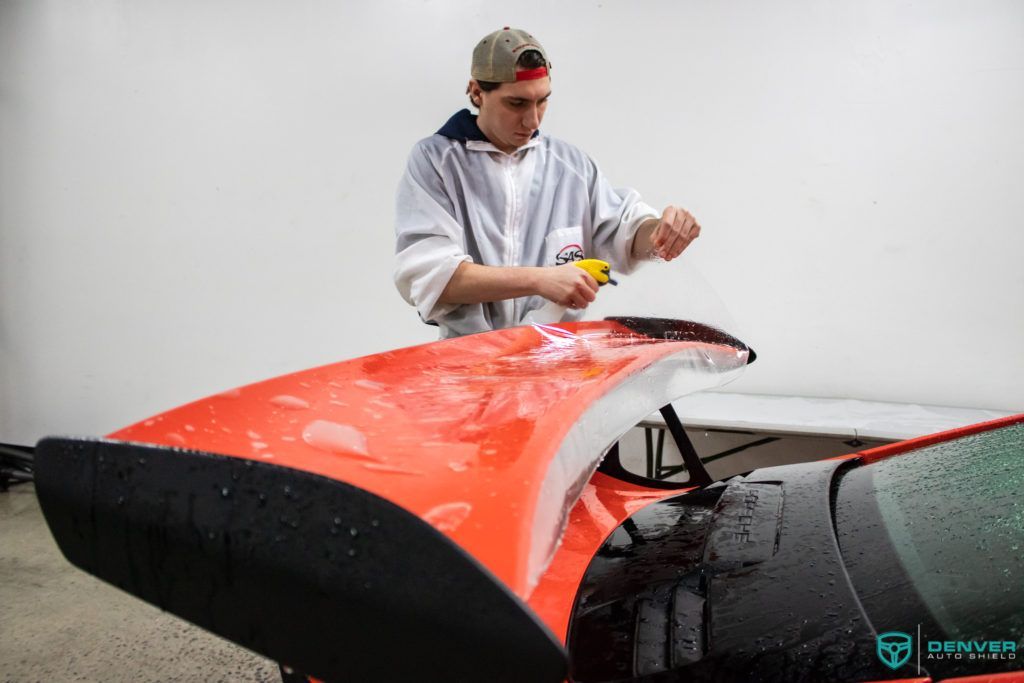 A man is polishing the hood of a red car.