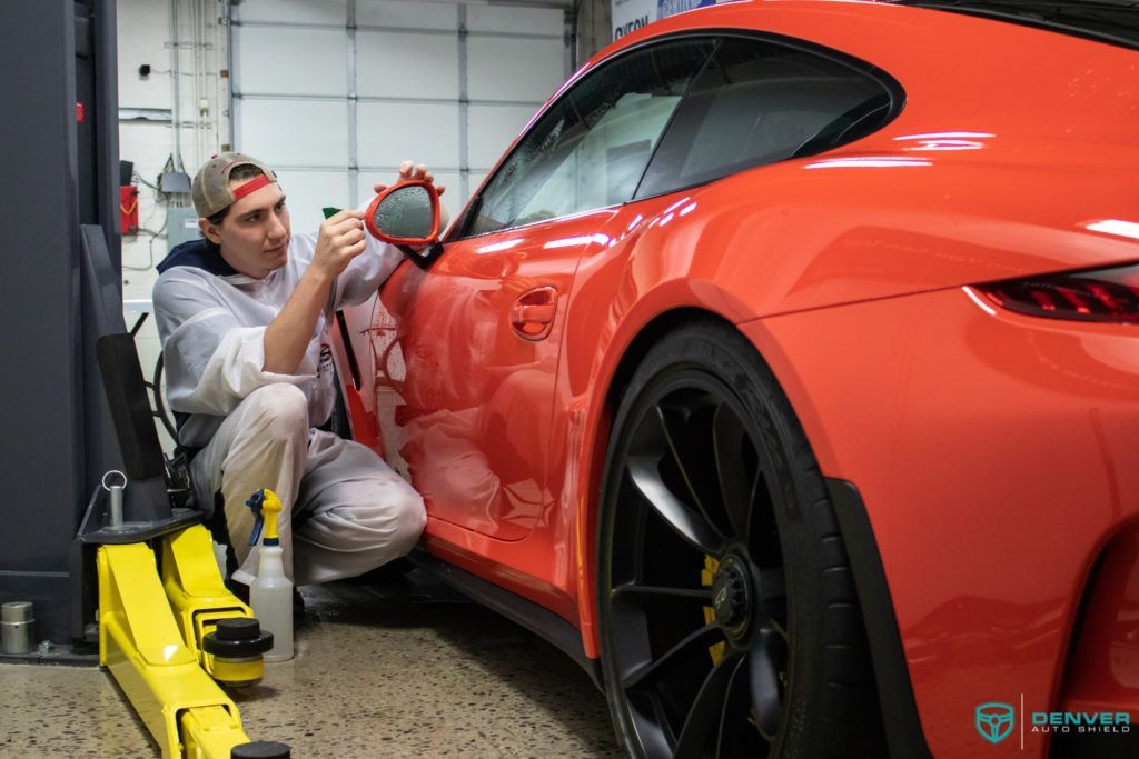 A man is cleaning a red sports car in a garage.