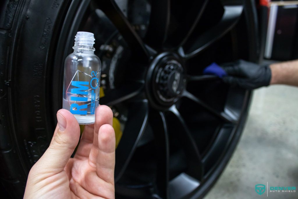 A person is holding a bottle of liquid in front of a car wheel.