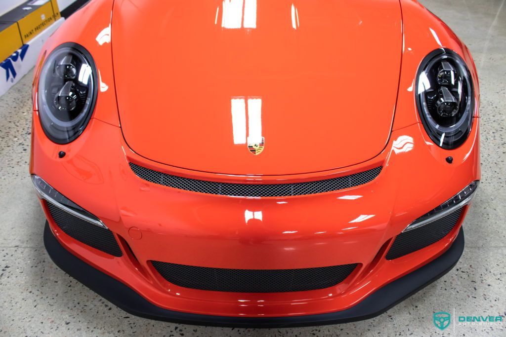 A close up of the front of an orange porsche