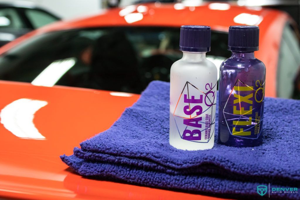 Two bottles of polish are sitting on a towel in front of a red car.