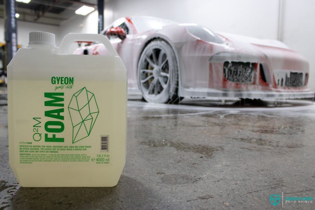 A bottle of foam is sitting next to a car covered in foam.