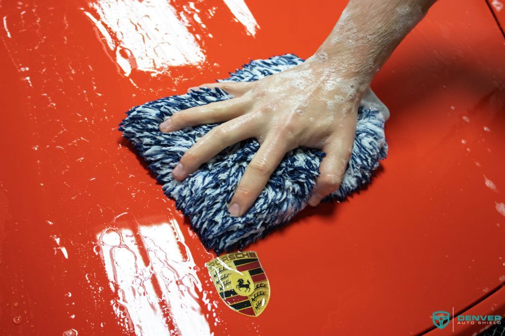 A person is cleaning a red car with a blue cloth.