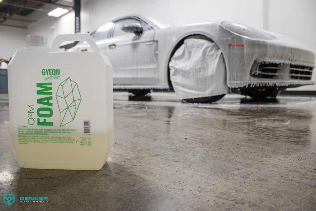 A white car is covered in foam next to a bottle of foam.