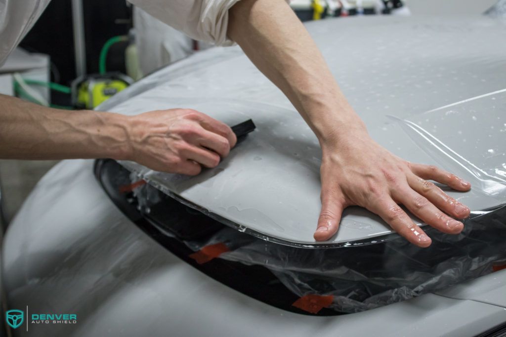 A man is applying a protective film to the hood of a car.