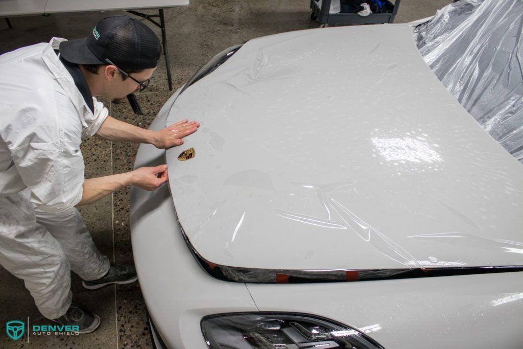 A man is wrapping the hood of a white car with plastic wrap.