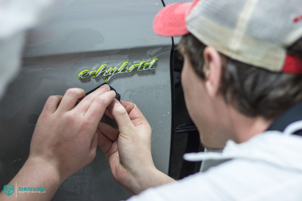 A man wearing a hat is applying a sticker to the side of a car.