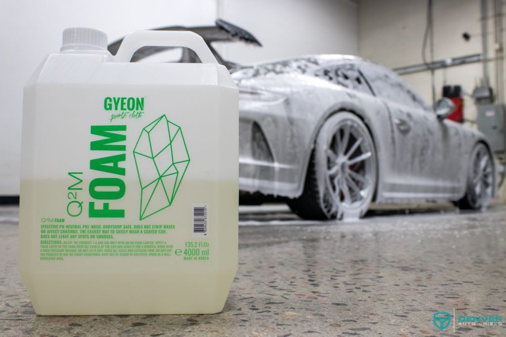 A bottle of foam is sitting next to a car covered in foam.