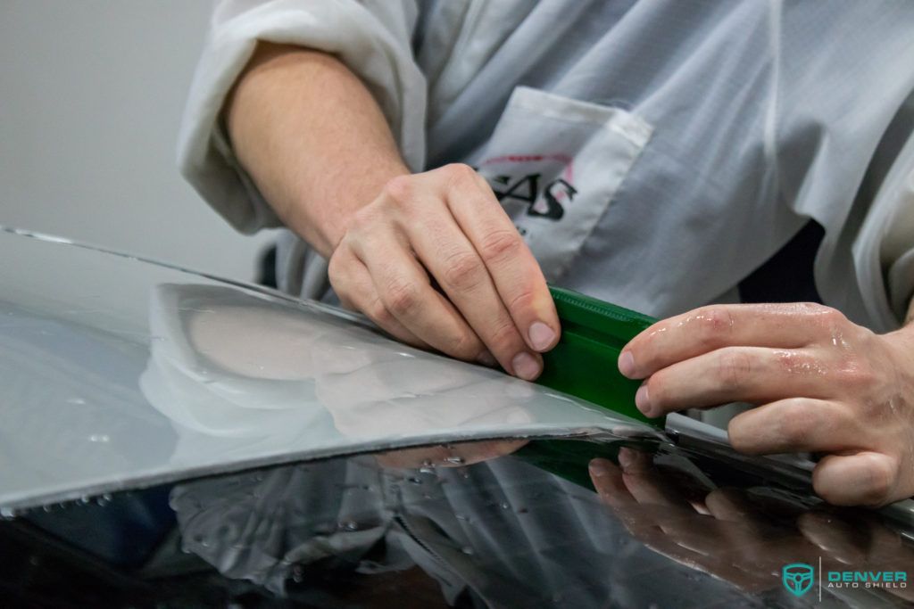 A person is applying a green tape to a car hood.