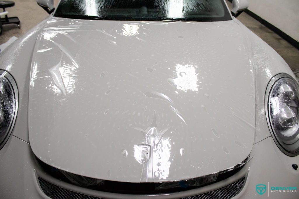 The hood of a white car is covered in plastic.