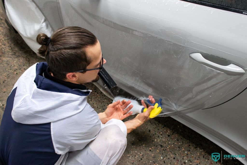 A man is applying a protective film to the side of a car.