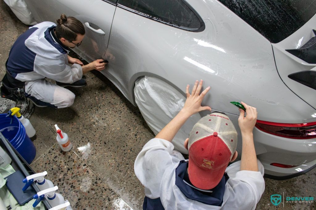 A man and a woman are wrapping a car in plastic.