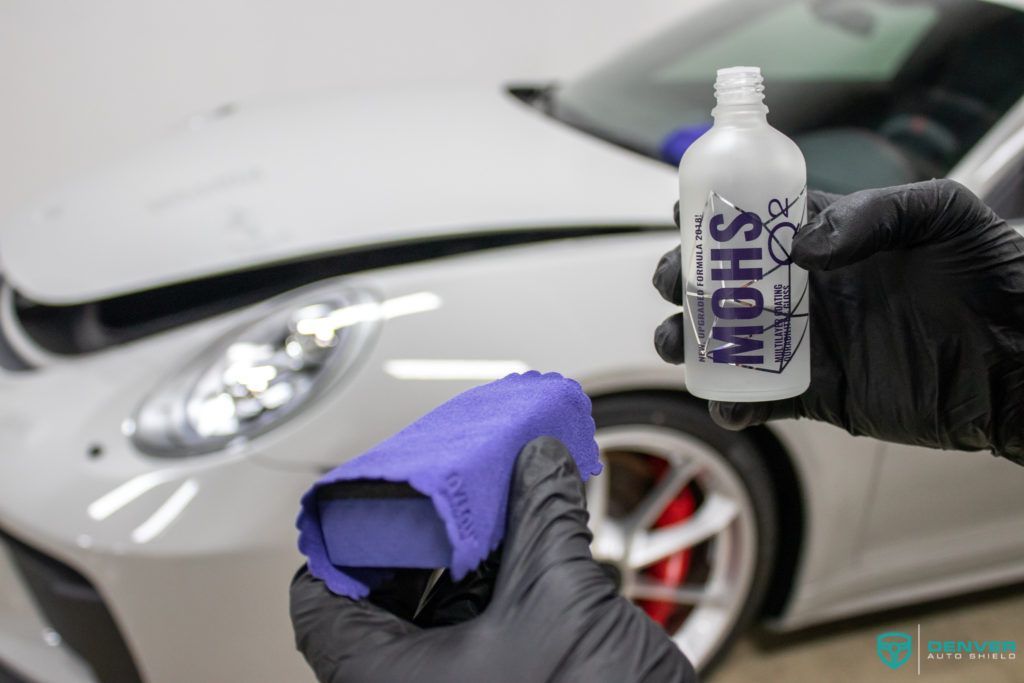 A person is holding a bottle of mohs in front of a white car.