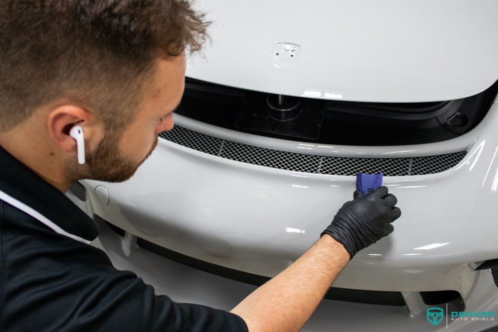 A man is cleaning the front of a white car.