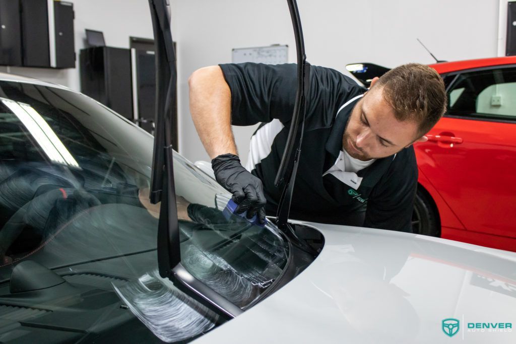 A man is cleaning the windshield of a car in a garage.