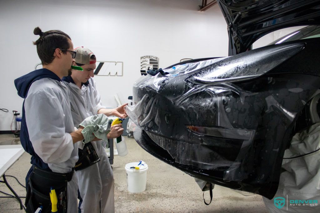 Two men are wrapping a car with plastic wrap in a garage.